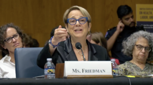 Karen Friedman, a woman with short blond hair and blue eyeglasses, speaks into a microphone at a Senate HELP Committee Hearing on July 17th.